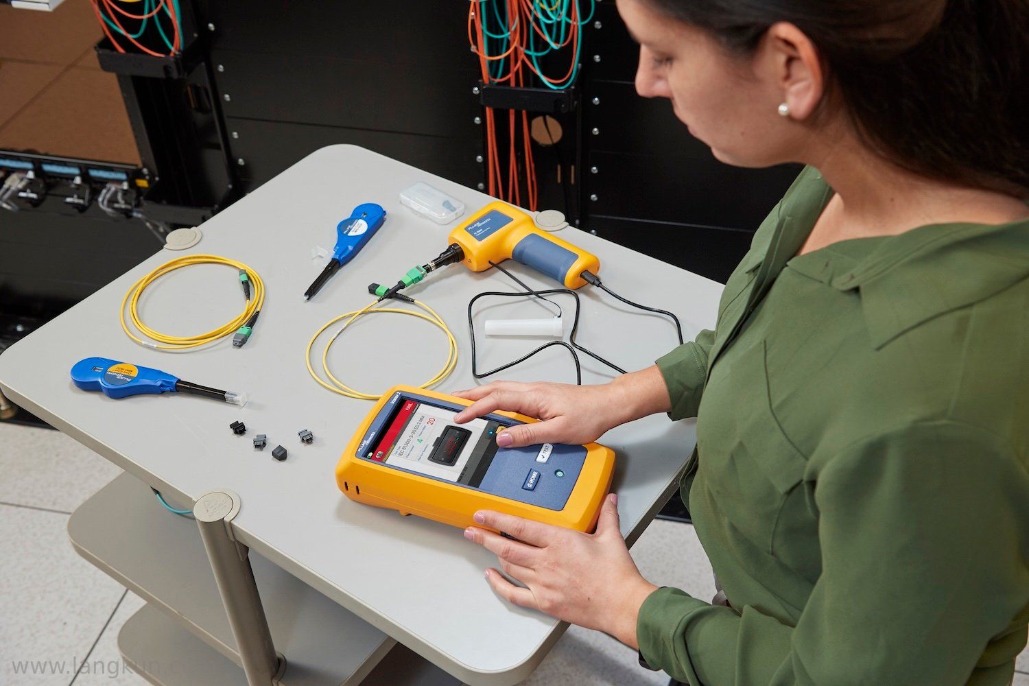 一位穿绿色衬衫的女士使用FI-3000 FiberInspector Pro检查一条刚清洁过的光纤电缆，该电缆放置在灰色桌面上